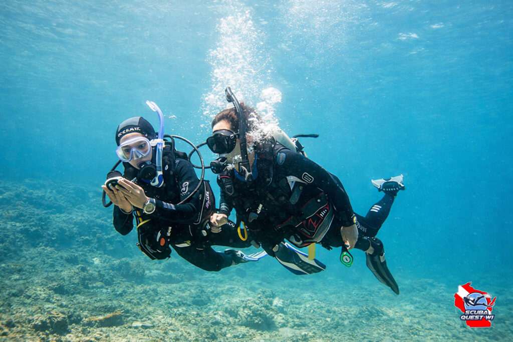 Two scuba divers swimming together underwater while one checks a dive navigation compass.